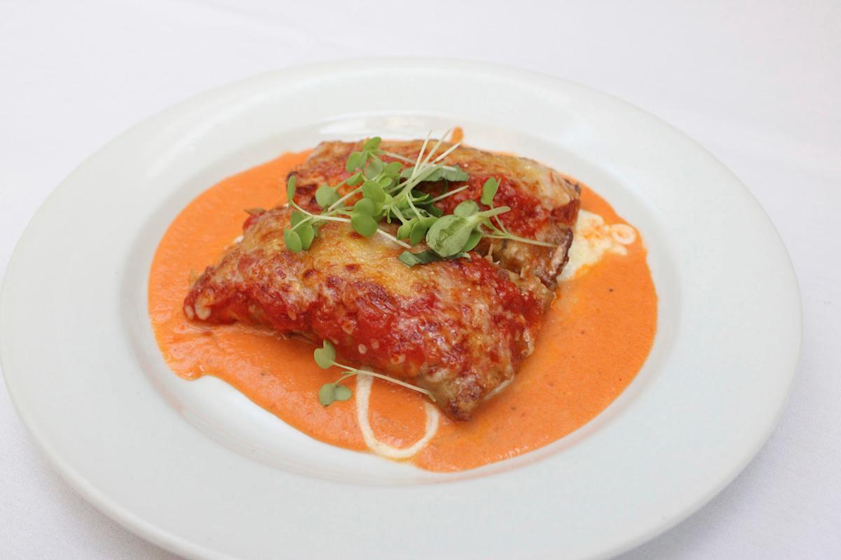 A plate of lasagna topped with melted cheese and garnished with microgreens, sitting in a pool of creamy tomato sauce on a white plate.