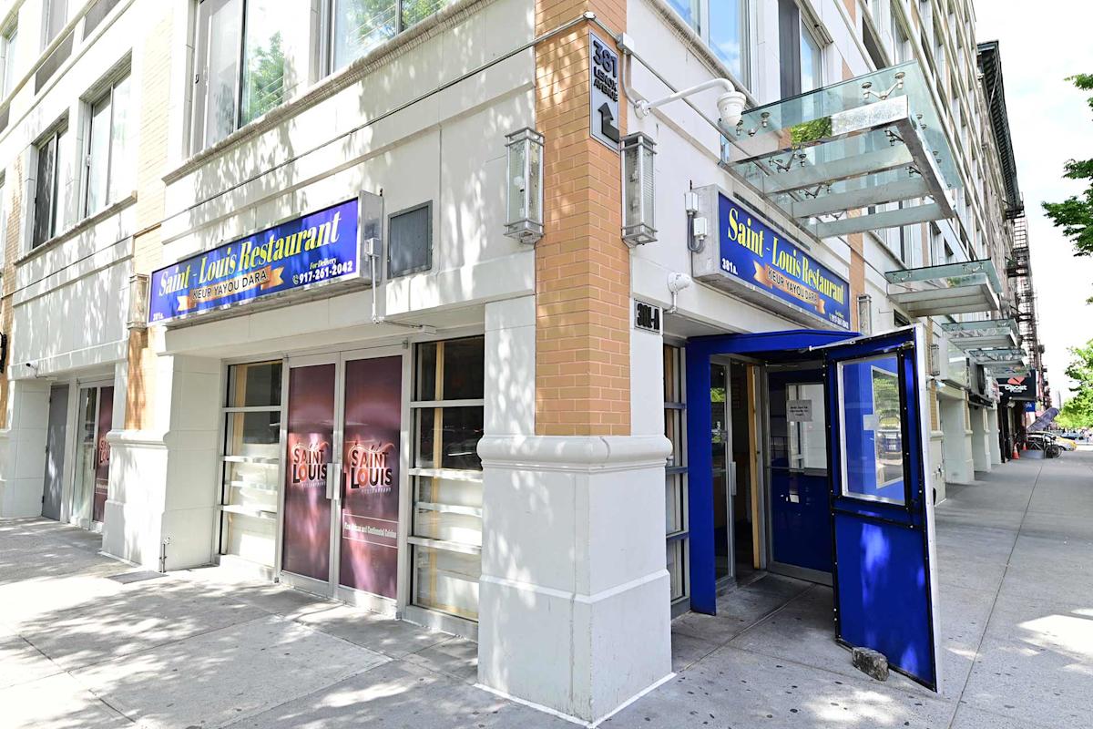 Street view of the Saint Louis Restaurant, with blue signage above the entrance and windows. The entrance door is open, and the building exterior features large windows and beige brick details.