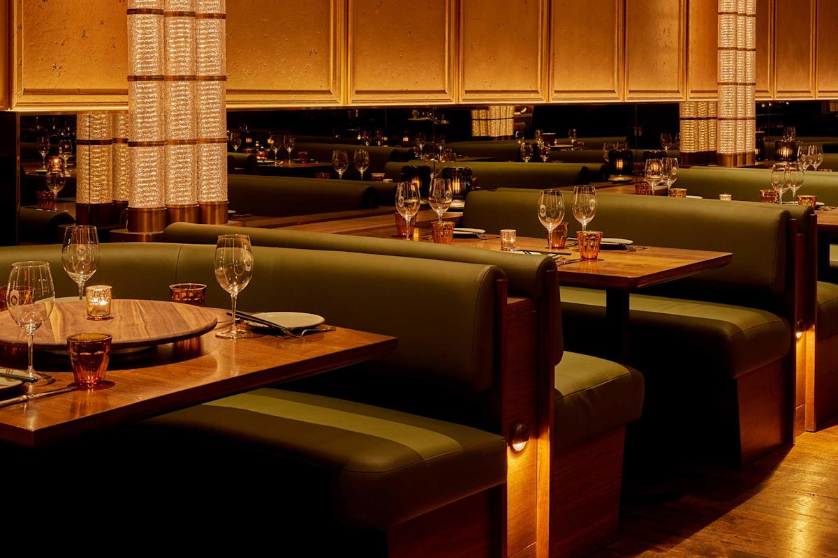 Dimly lit restaurant interior with green leather booths, set wooden tables, wine glasses, amber water glasses, plates, and soft ambient lighting creating a warm and intimate atmosphere.