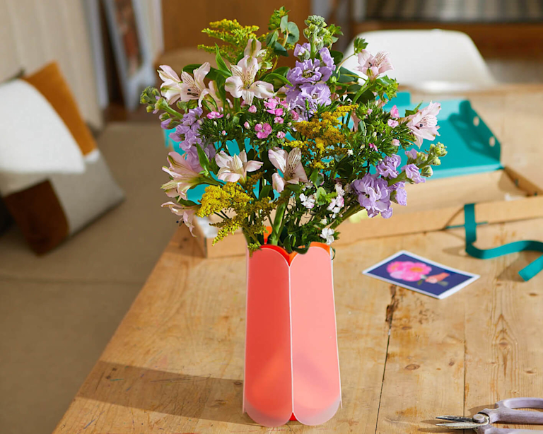 A bunch of spring flowers in a bright coral letterbox vase.