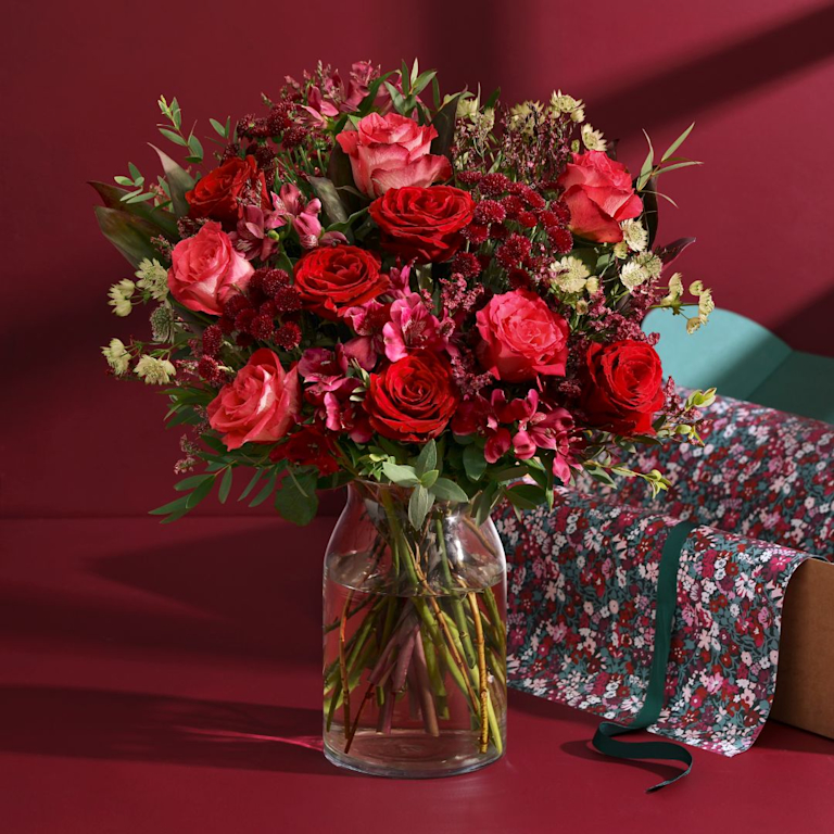 A textured, elegant bouquet with richly shaded roses, alstroemeria and astrantia. An open box, lined with a Liberty print, is positioned behind.