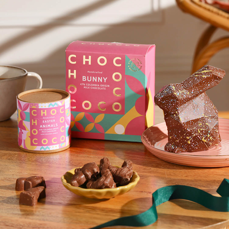 A geometric, milk chocolate Easter bunny with a playful paint-splatter design, alongside a box of solid chocolate mini-animals.