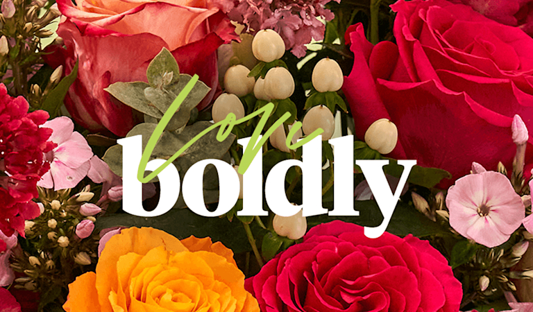 A close-up of vivid orange and deep pink roses, with the phrase 'Love boldly' over the top