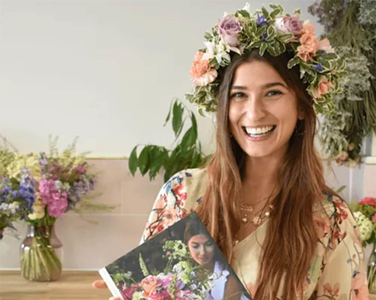 Die Londoner Autorin und Designer-Floristin Rowan Blossom, mit ihrem Bestseller-Buch 'Living with Flowers' in der Hand und einem Blumenkranz auf dem Kopf.