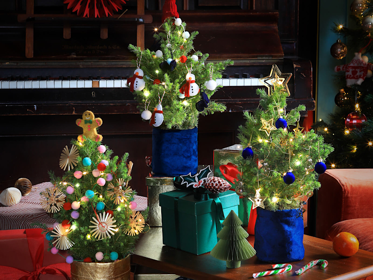 Eine Reihe von niedlichen kleinen Weihnachtsbäumchen. Jeder von ihnen ist individuell mit leuchtenden Lichterketten, Girlanden und Ornamenten geschmückt.