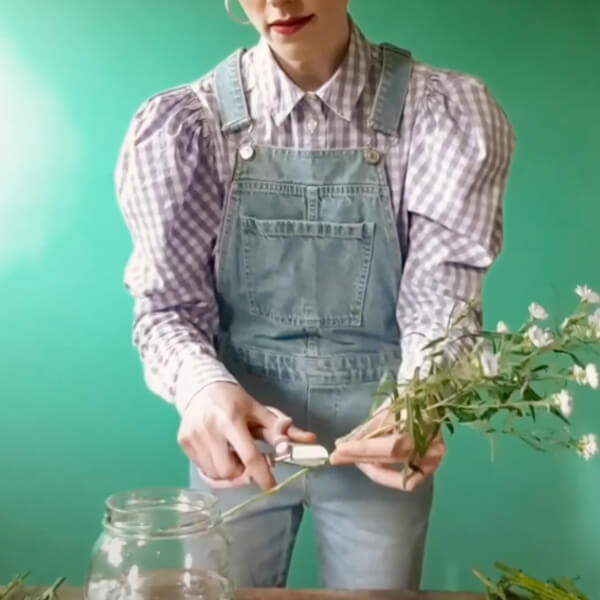Harriet holds a flower stem in front of her and cuts the end.