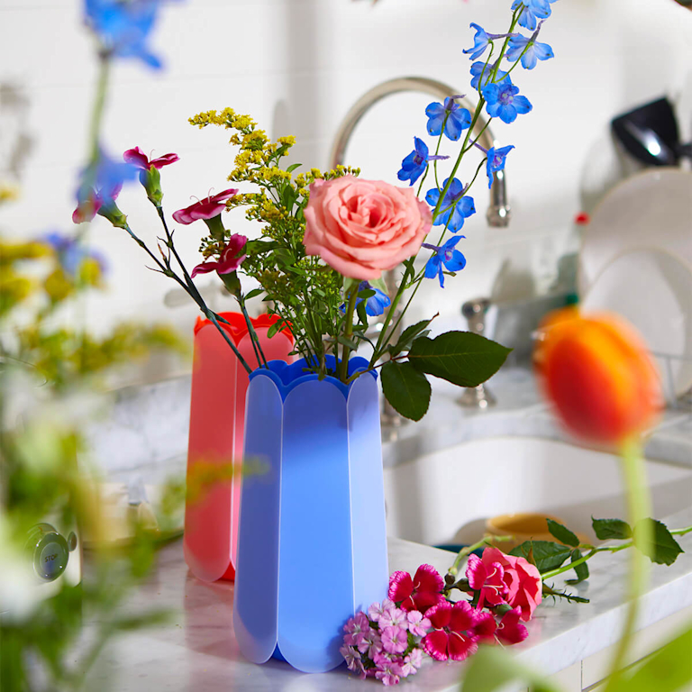 A selection of seasonal flowers in different colours, in a pop-up vase next to a kitchen sink.