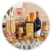 Christmas hamper spread with a bottle of red wine, crackers, breadsticks, olives, chutney and other festive treats on a rustic cloth.