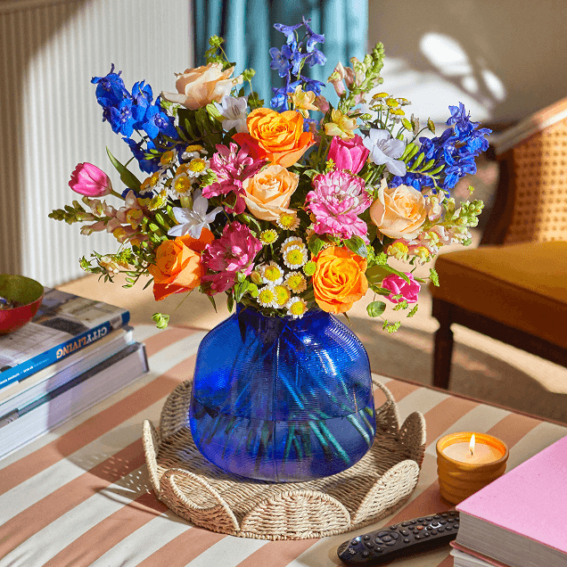 Bloom & Wild bouquet made up of Pink, Orange, Blue and Yellow flowers in a blue glass vase