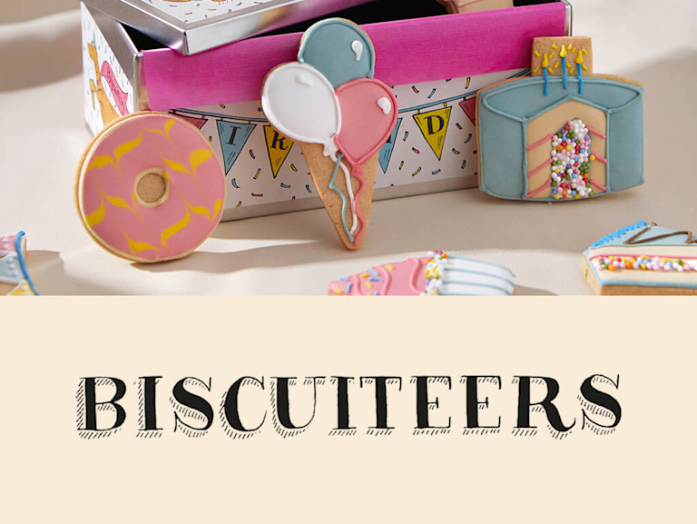 Two images. The first shows a mix of iced biscuits, decorated to look like party items (i.e balloons and birthday cake), placed around a celebratory tin. The second is of Biscuiteers' logo on a linen background.