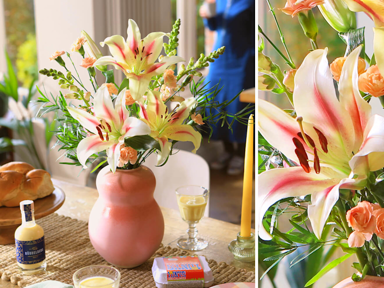 Ein prächtiger Blumenstrauß mit edlen Lilien. Daneben sind bunt verpackte Schokoeier und Eierlikör zu sehen.