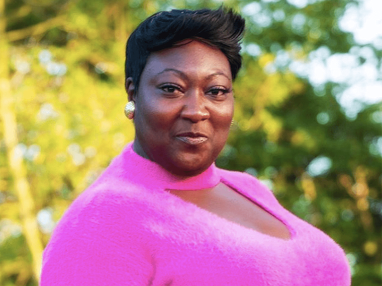Phyllis, a dark-skinned woman with a fierce pixie cut and a quiff, wears a hot pink jumper.