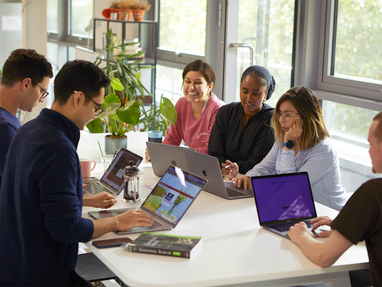 Eine Gruppe von Arbeitskolleginnen und Kollegen sitzen mit ihren Laptops gemeinsam an einem Tisch