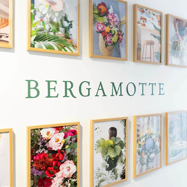 A wall displaying different framed photos of Bergamotte flowers and plants, with the Begramotte logo in the middle.
