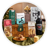 A wicker hamper filled with a bottle of red wine, biscuits and boxed festive treats.