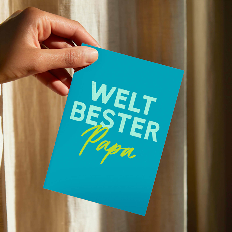 Eine Hand hält eine Grußkarte mit der Aufschrift „Weltbester Papa”