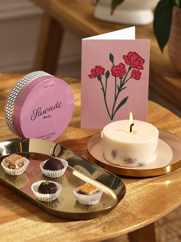 A hand lights a candle. It's surrounded by its packaging, reading glasses and other homeware.