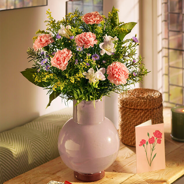 Ein Blumenstrauß in sanften Farbtönen steht in einer Keramikvase auf der Konsole