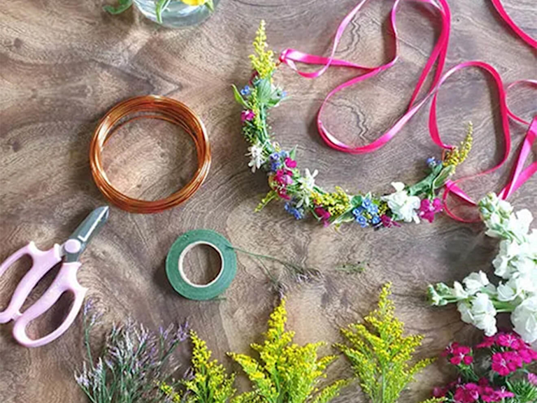 Ein Blumenkranz umgeben von einer Floristenschere, Klebeband und weiteren Bastelutensilien