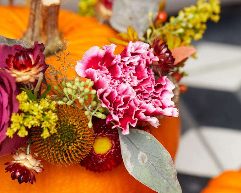 A flower crown of pink carnations and dried stems adorns a large pumpkin.