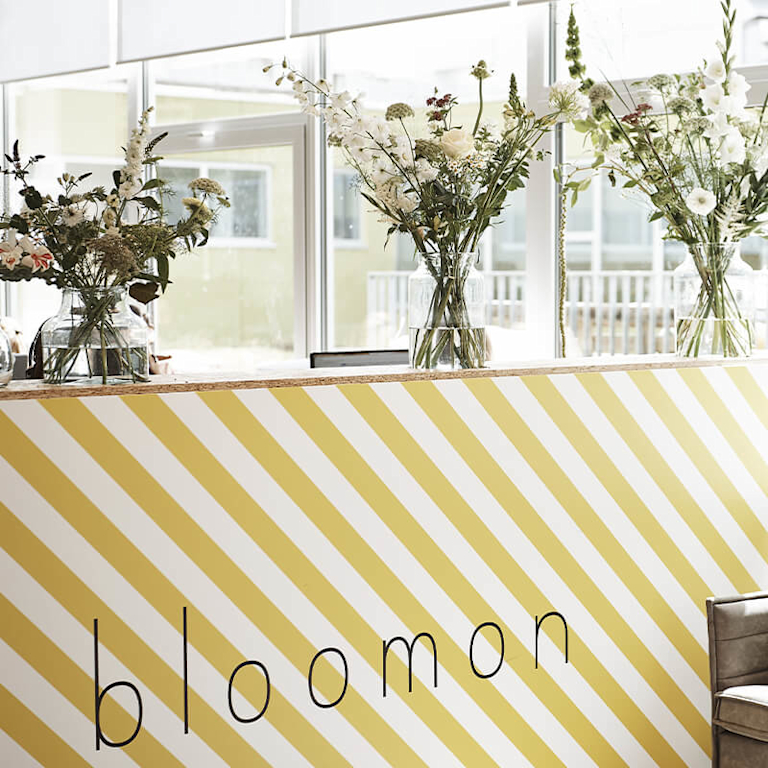 A reception desk at bloomon HQ, decorated in yellow and white stripes. On the counter are three vases of beautiful, architectural bloomon bouquets.