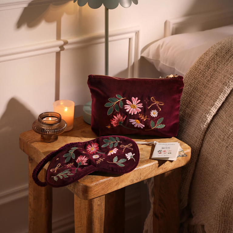 A Bloom & Wild Hamper Velvet pouch and eyemask on a bed side table