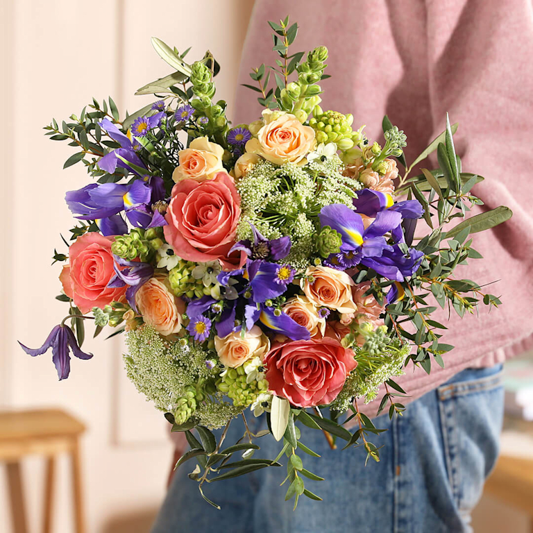 An elegant, multi-tonal bouquet featuring peach and coral roses, deep purple irises and trailing eucalyptus.