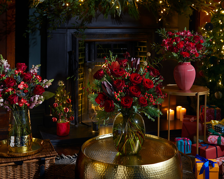 A room with gold tables and an open fireplace, full of Christmassy flowers.