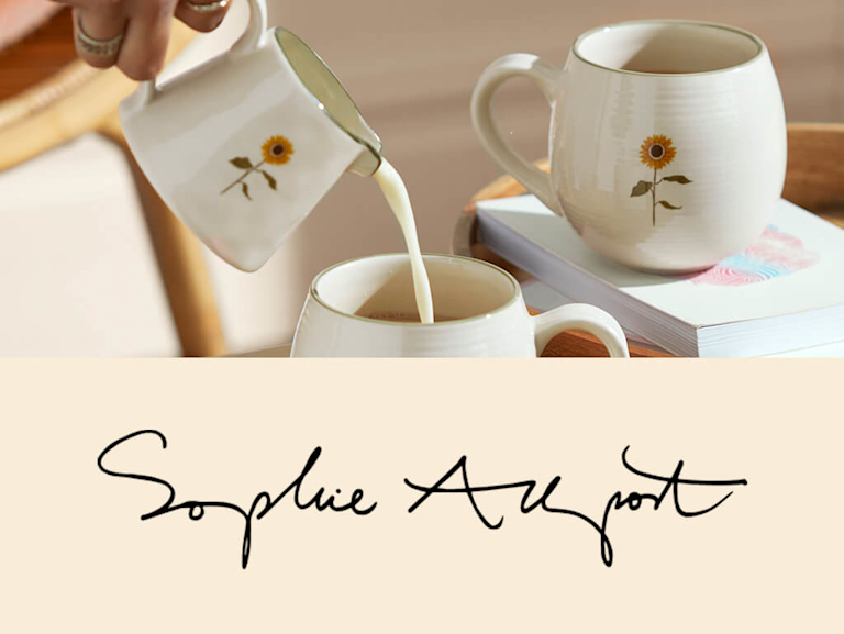 Two classy white ceramic mugs and a milk jug, with a simple and stylish sunflower painted on them.