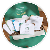 An open green letterbox gift box showing greeting cards and wellbeing treats inside.