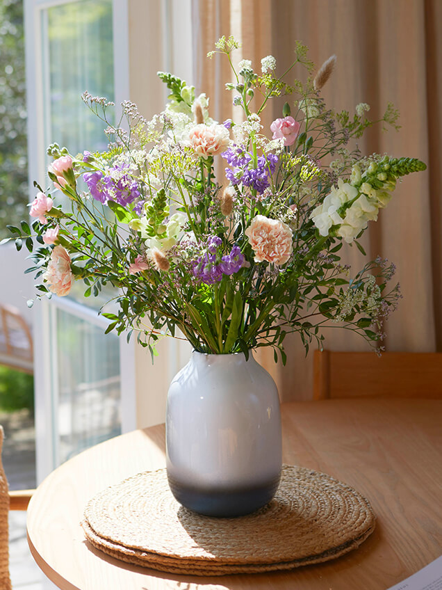 Hands reach into letterbox packaging, where sunny yellow-toned stems lay.