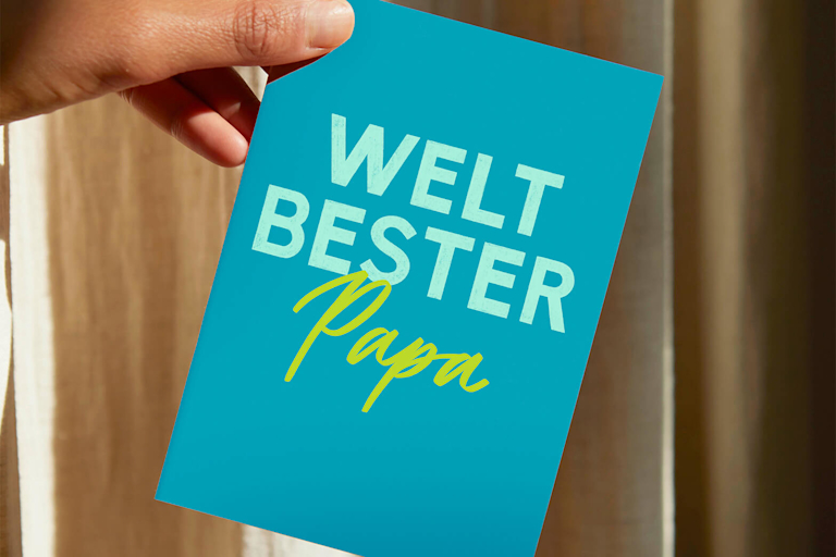 Eine Hand hält eine Grußkarte mit der Aufschrift „Weltbester Papa”