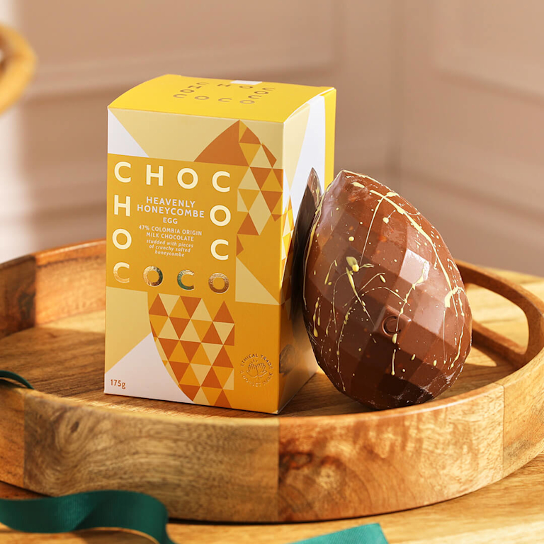 A milk chocolate Easter egg with a yellow chocolate drizzle, standing beside a bold yellow and gold honeycomb-themed gift box.