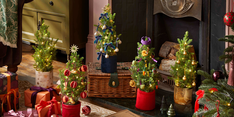 Mini Christmas trees are dotted around a living room. In between them are festive snacks, lit candles and an embroidered stocking.