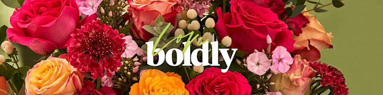 A close-up of vivid orange and deep pink roses, with the phrase 'Love boldly' over the top