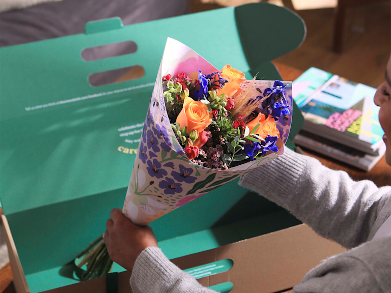 Ein mit Blumenpapier verpackter Strauß wird gerade aus der Box genommen