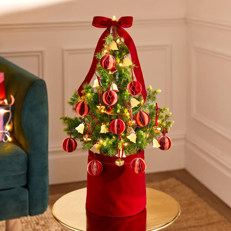 A larger Tiny Tree with hanging bells, honeycomb baubles and a jingle bell garland in a burgundy velvet pot.