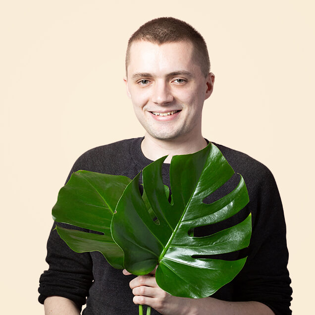 Jamie is a white man in his thirties. He holds up two monstera leaves.