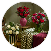 Bouquets of red roses and white flowers in vases on a table beside a green gingham cloth.