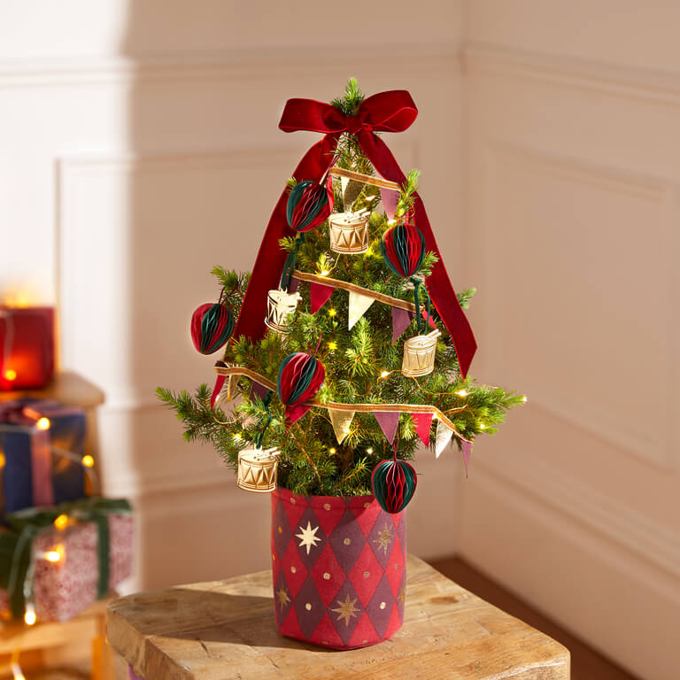 A Tiny Tree decorated with metal drums, honeycomb baubles and bunting in a harlequin-print pot.
