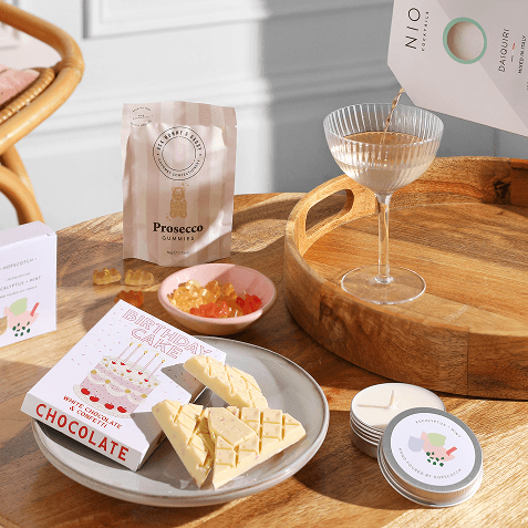A selection of hamper items including a candle, birthday cake chocolate, a cocktail mix, and gummy bears.