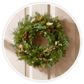A Christmas wreath of fir and dried winter flowers hanging on a white front door.