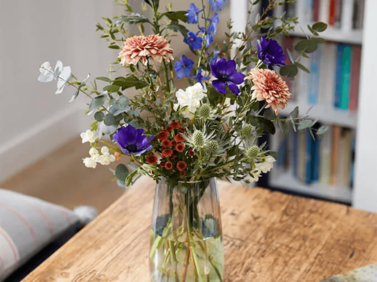 Two images side by side: the first shows individually wrapped stems and a booklet of styling tips; the second shows a large bouquet arranged in a vase, with yellow, orange and blue stems.