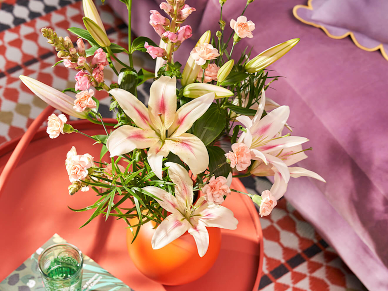 Ein üppiger Blumenstrauß in einer pinken Vase steht auf dem Couchtisch
