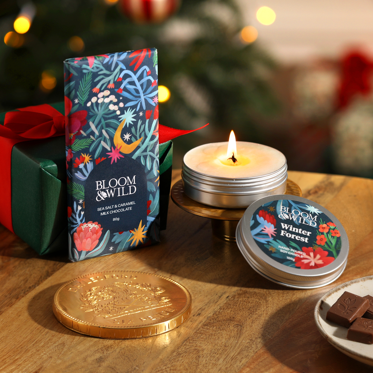 A Bloom & Wild Chocolate Bar, Candles and gold Coin sit upon a wooden table.