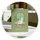 A sage green illustrated greeting card standing upright on a table.