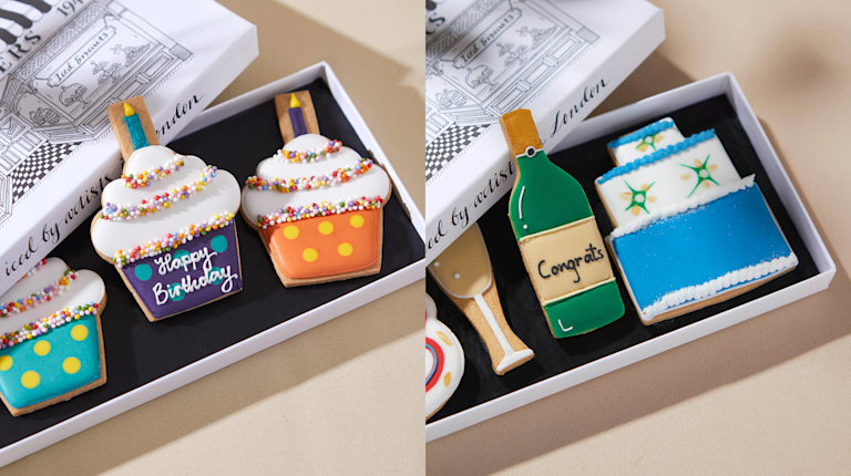 A number of iced biscuits sit in their boxes. The ones on the right have been designed to look like cupcakes while those on the left look like party items (a bottle of sparkling wine, a tiered cake and a champagne flute).