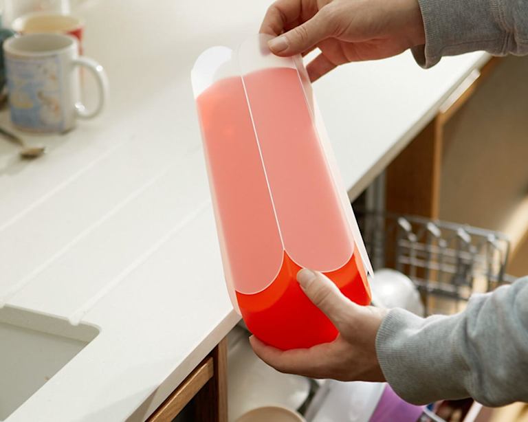 A woman pulls off a plastic sheath from a letterbox vase, next to an open dishwasher