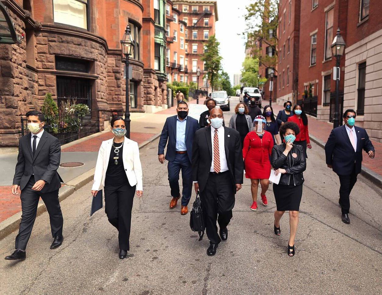 A group of state and local representatives walking in downtown Boston with masks.