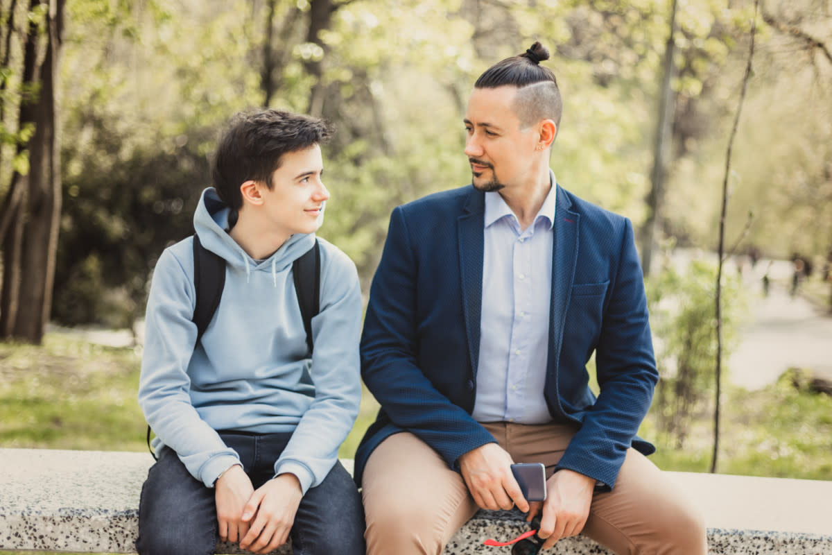 Un père et son fils discutent assis sur un banc de parc